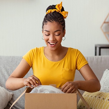 Woman in yellow shirt opening a box on her sofa