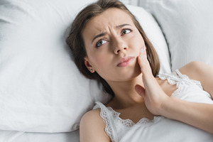 Woman with tooth pain lying in bed looking concerned